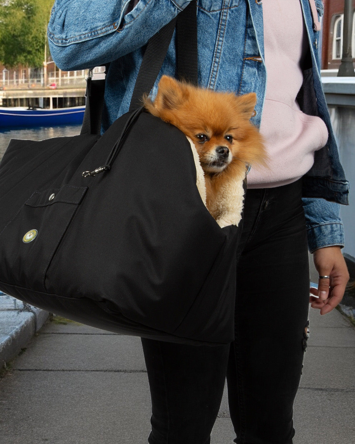 Ein Mann trägt eine Soho Poms Hundetragetasche mit einemzwergspitz darin.